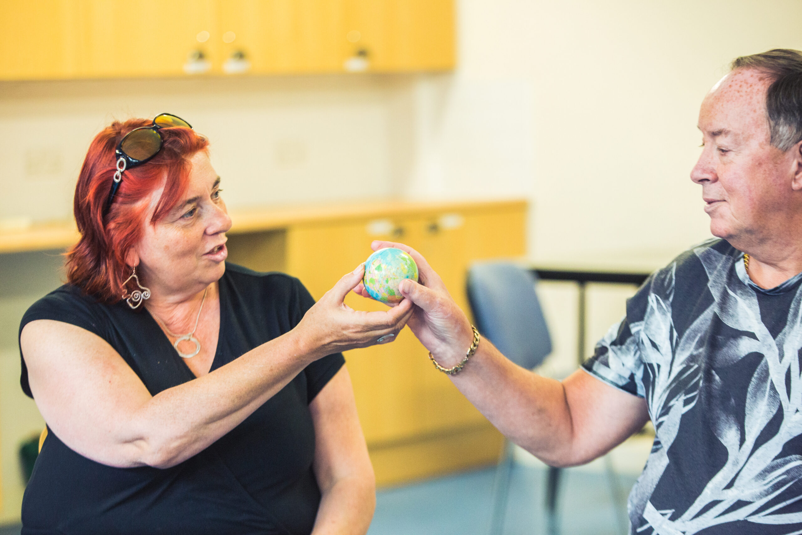 A photo of two people passing a small toy globe between them, mid-conversation, smiling.